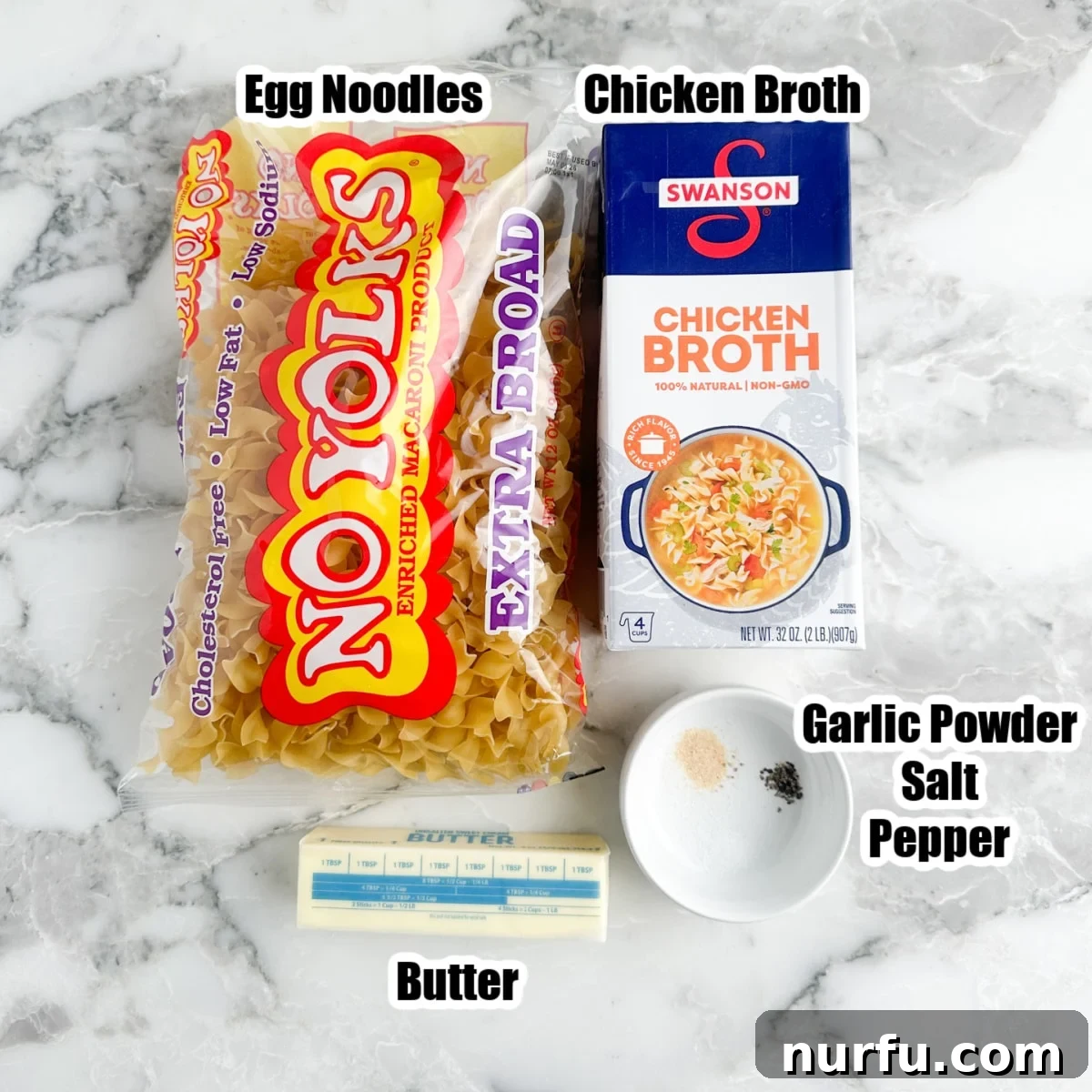 Simply Perfect Buttered Noodles 2 Collection of key ingredients for buttered noodles: dry egg noodles, a carton of chicken broth, sticks of butter, and a small dish of seasonings including garlic powder, salt, and pepper.
