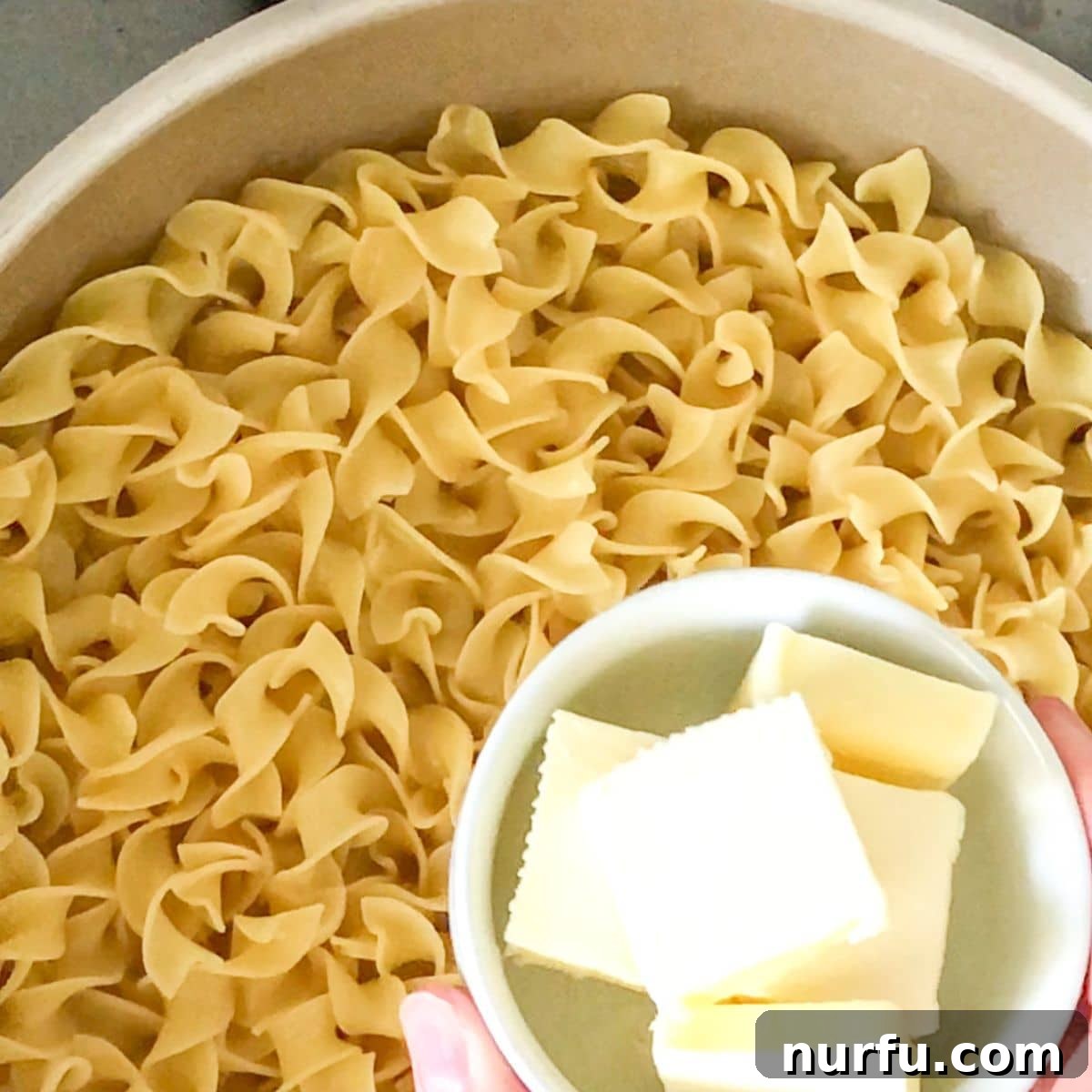 Simply Perfect Buttered Noodles 4 Egg noodles being added to a pot of boiling chicken broth and butter, ready to cook.
