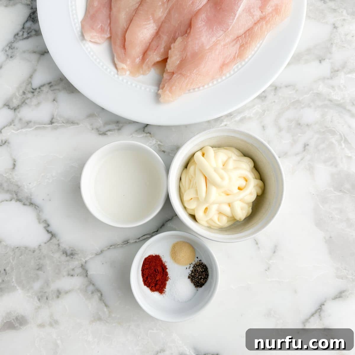 Tenderizing Mayonnaise Chicken Marinade 3 A visual display of the simple ingredients needed for this recipe: raw chicken breasts, a bowl of pickle juice, a jar of creamy mayonnaise, and various seasonings, ready for mixing.