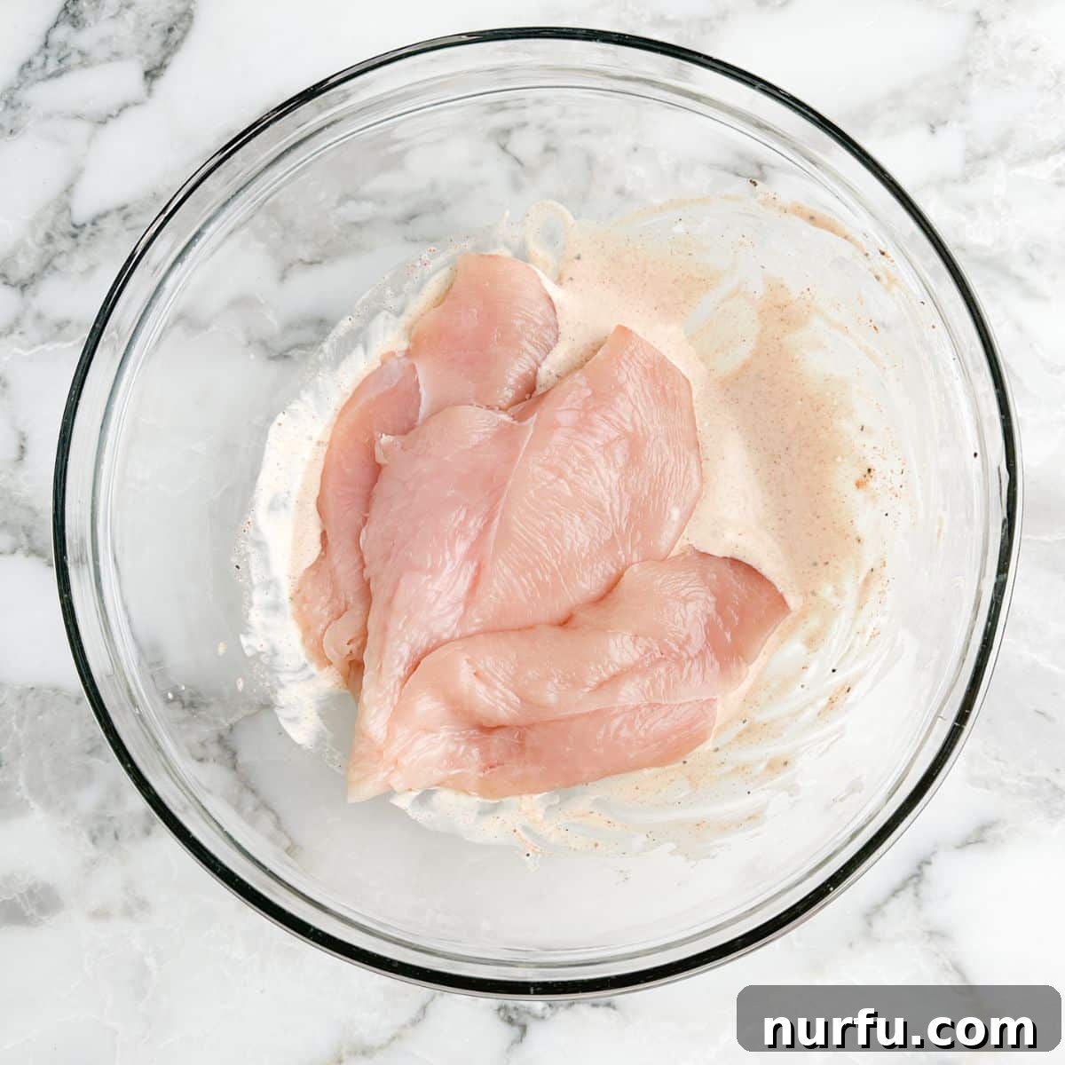 Tenderizing Mayonnaise Chicken Marinade 5 Raw chicken pieces are thoroughly coated in the creamy mayo marinade within a mixing bowl, ensuring every surface is imbued with flavor.
