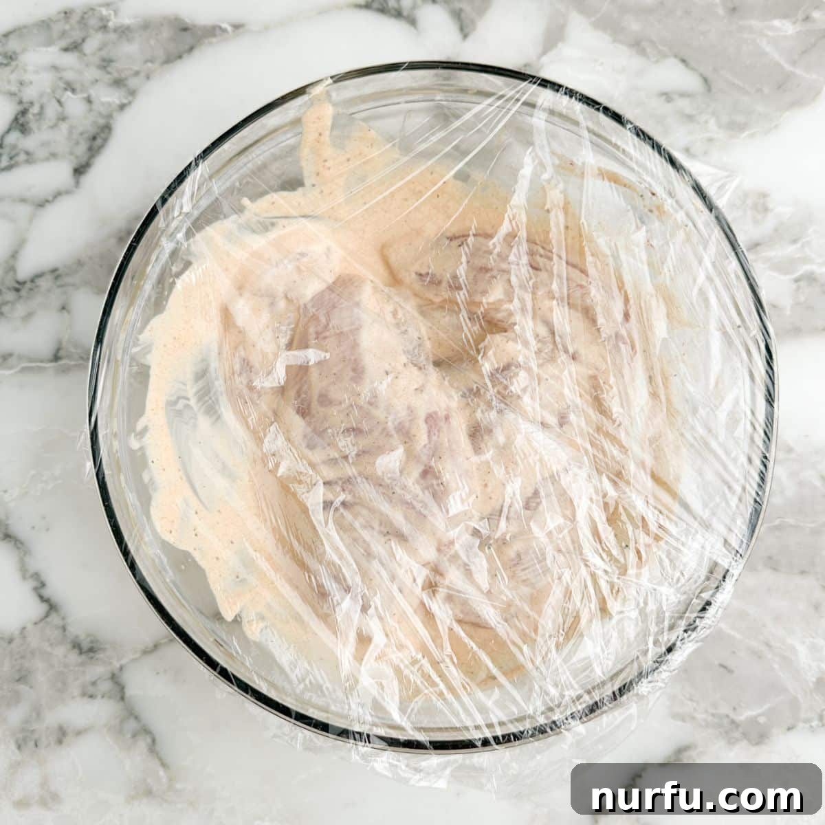 Tenderizing Mayonnaise Chicken Marinade 6 Uncooked chicken pieces sit immersed in the creamy marinade within a bowl, ready to absorb all the delicious flavors during refrigeration.
