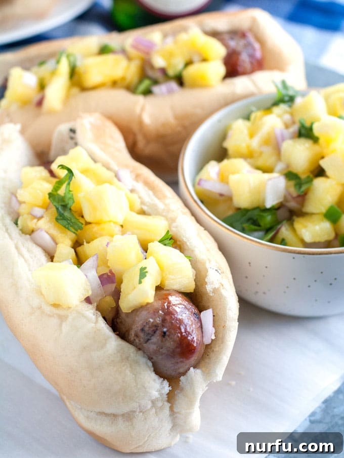 bratwurst and pineapple salsa A close-up shot of grilled bratwursts nestled in buns, generously topped with fresh pineapple salsa.