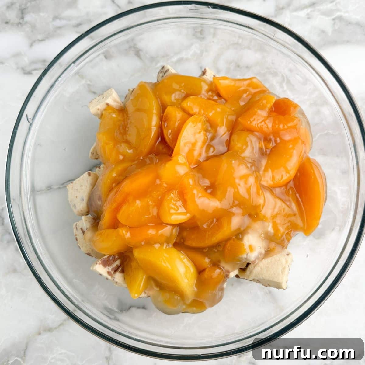 Peachy Cinnamon Swirl Cobbler 5 A large bowl containing cut cinnamon roll pieces with peach pie filling poured over them.