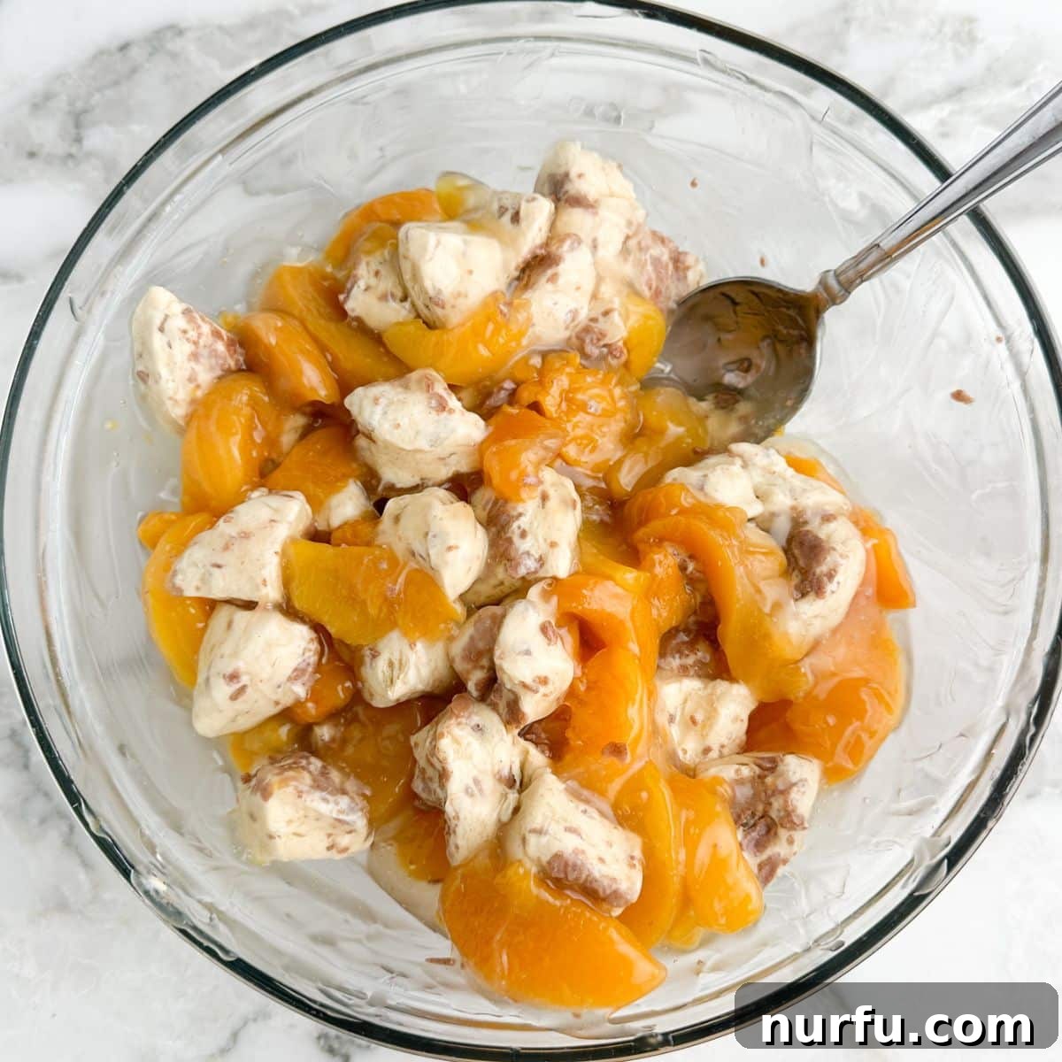 Peachy Cinnamon Swirl Cobbler 6 Close-up of a bowl showing quartered cinnamon rolls thoroughly mixed with peach pie filling.