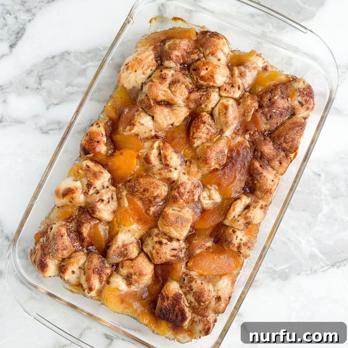 Peachy Cinnamon Swirl Cobbler 8 A baked cinnamon roll peach cobbler, golden brown and bubbly, in a casserole dish.