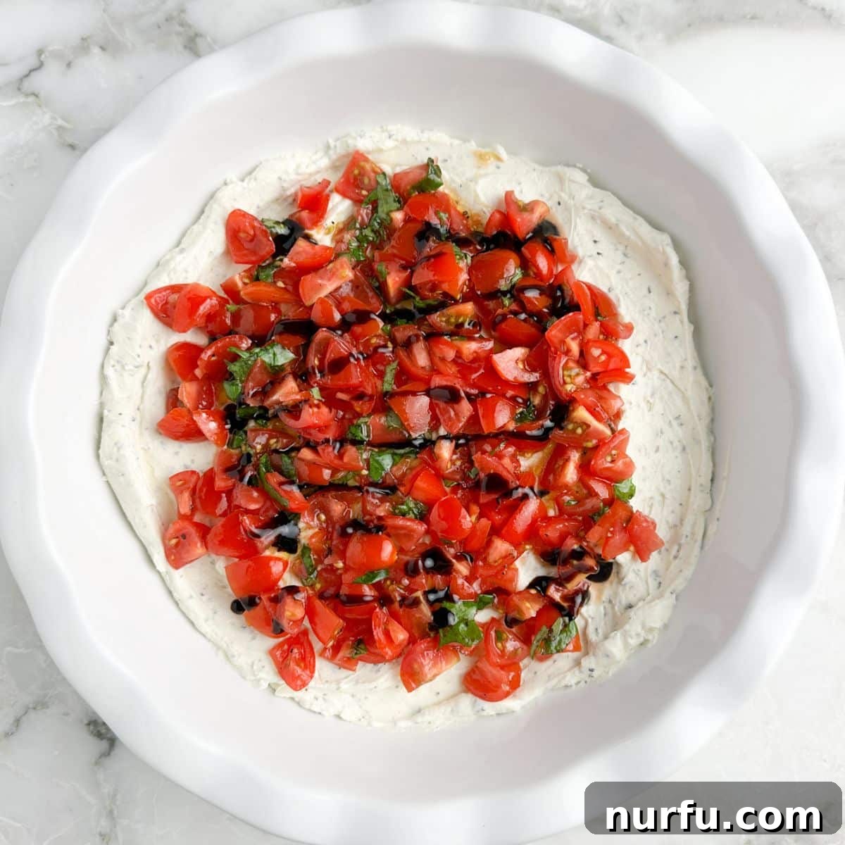 Sun-Kissed Bruschetta Topping 7 A beautifully presented dish of bruschetta dip, featuring a creamy white base generously topped with a vibrant red tomato and basil mixture, finished with a luscious drizzle of dark balsamic glaze.