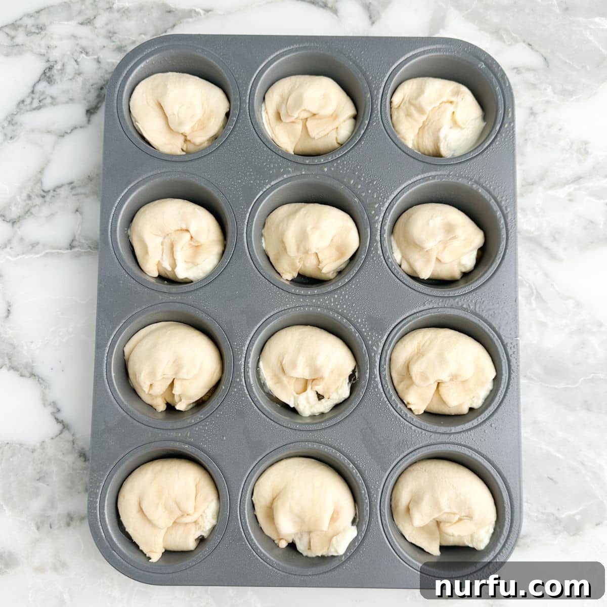 Flaky Peach Cheesecake Delights 6 Muffin tin filled with uncooked mini peach crescent cheesecakes, with dough folded over and sealed.