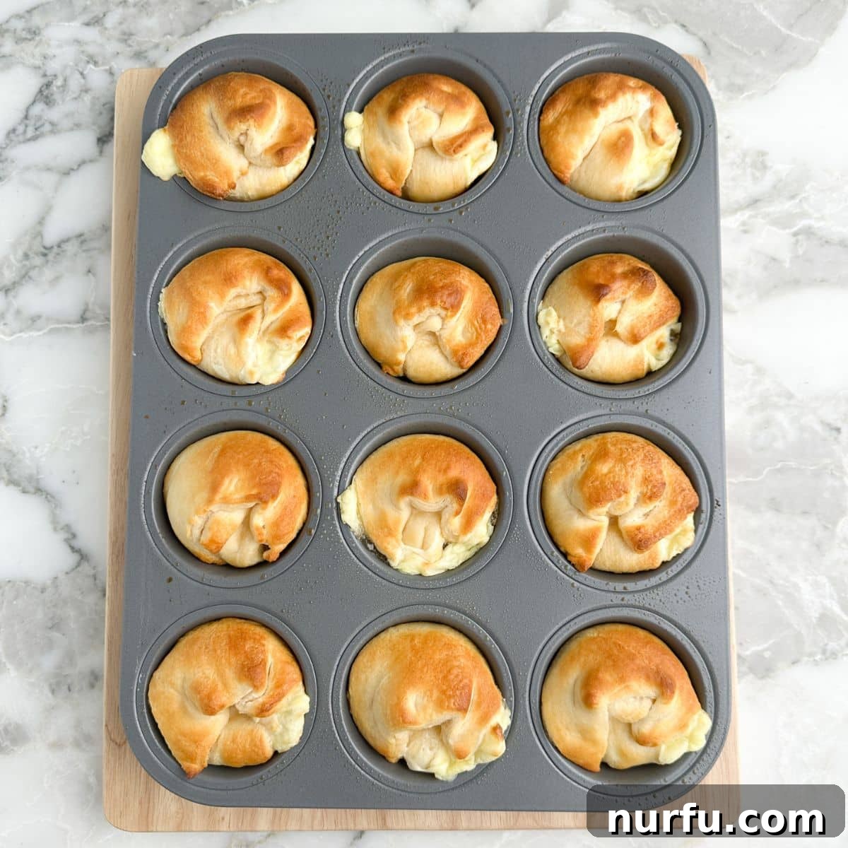 Flaky Peach Cheesecake Delights 7 Muffin tin with cooked, golden-brown peach crescent cheesecakes.