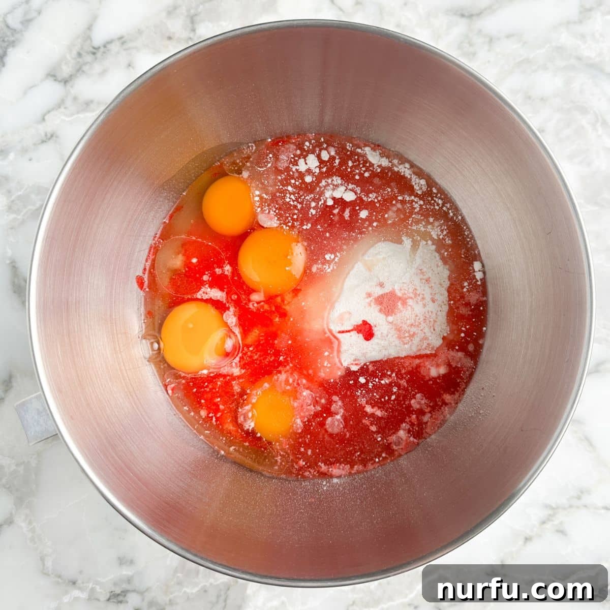 A mixing bowl filled with chopped strawberries, eggs, cake mix, and oil, ready to be combined.