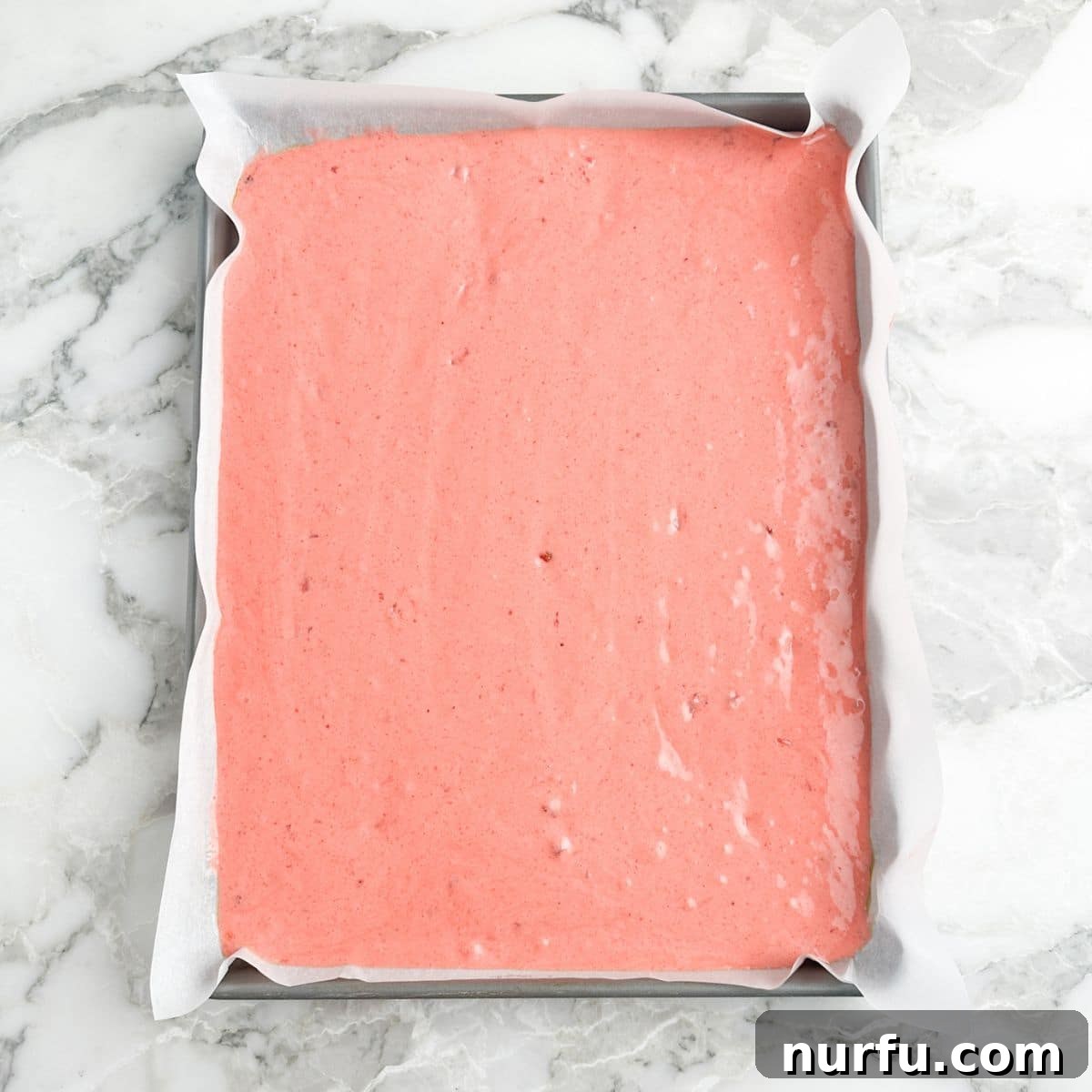 Sheet pan with strawberry cake batter spread evenly, ready for the oven.