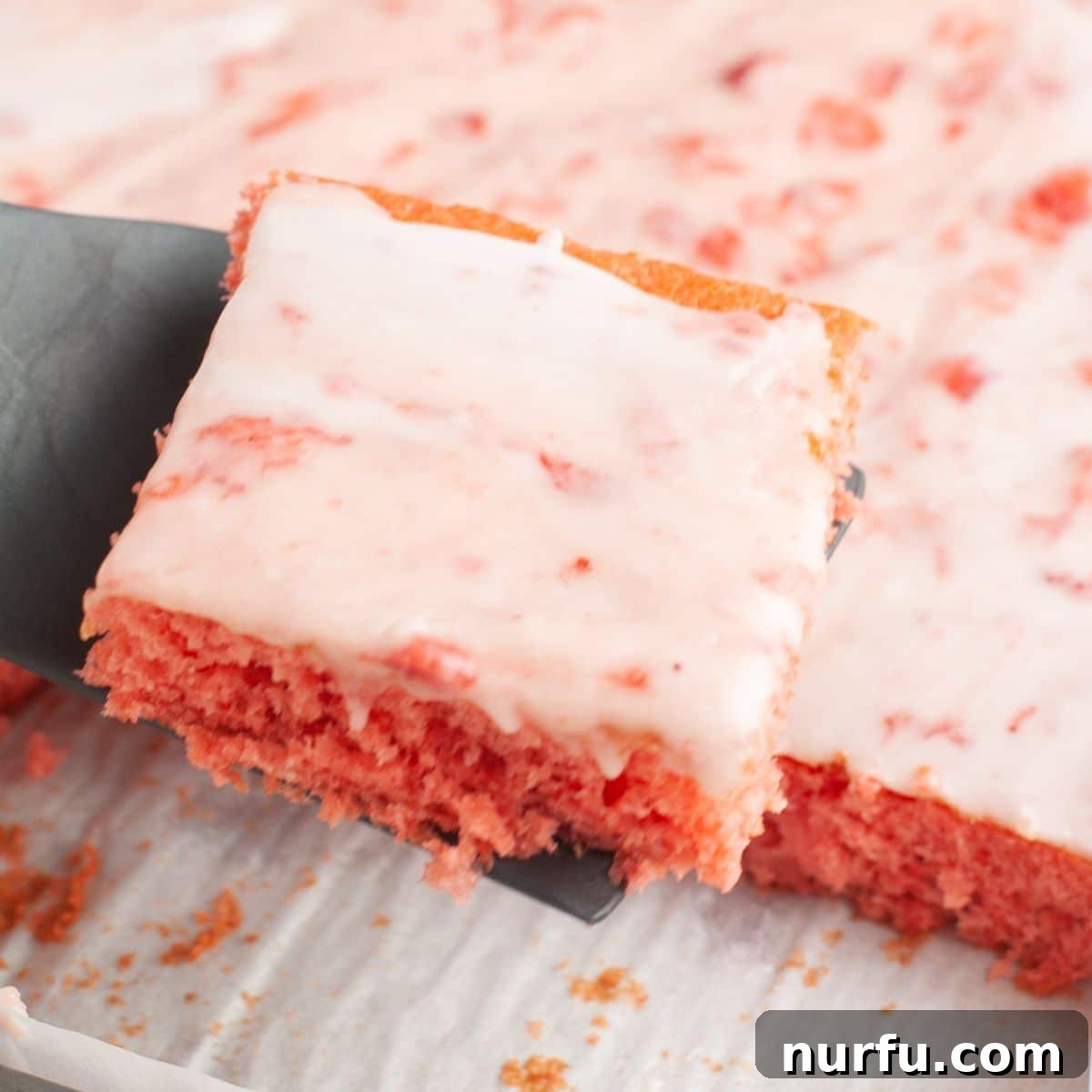 A spatula lifting a perfect piece of strawberry sheet cake, showing the moist crumb and generous icing.