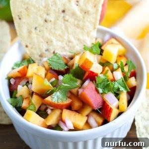 A beautifully presented bowl of fresh peach salsa with a tortilla chip, ready to be enjoyed.