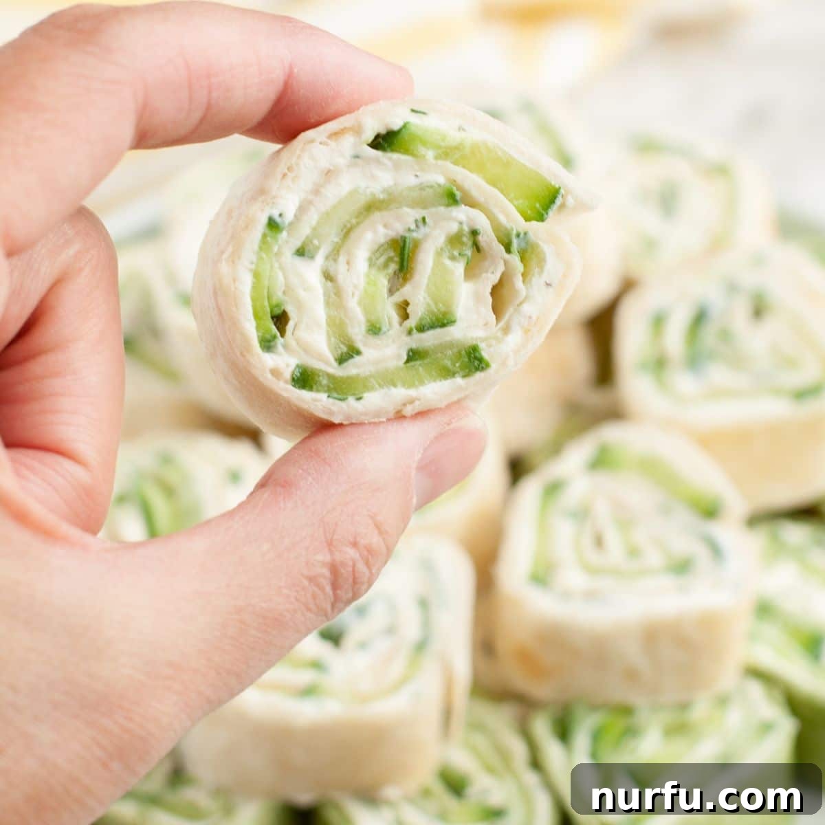 A hand gracefully holding a single, perfectly sliced cucumber pinwheel, highlighting its appealing layers.