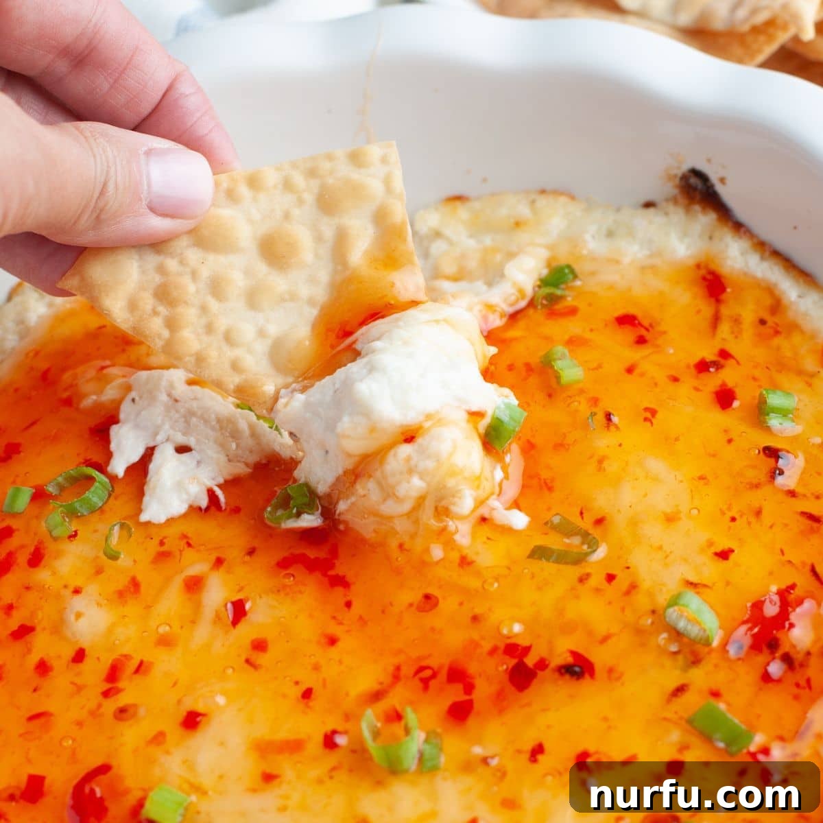 Irresistible Crab Rangoon Dip 2 Baking dish with crab rangoon dip and chip dipping into it.