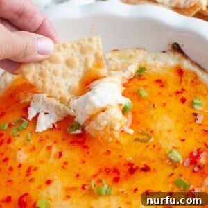 Irresistible Crab Rangoon Dip 8 Baking dish with crab rangoon dip and chip dipping into it.