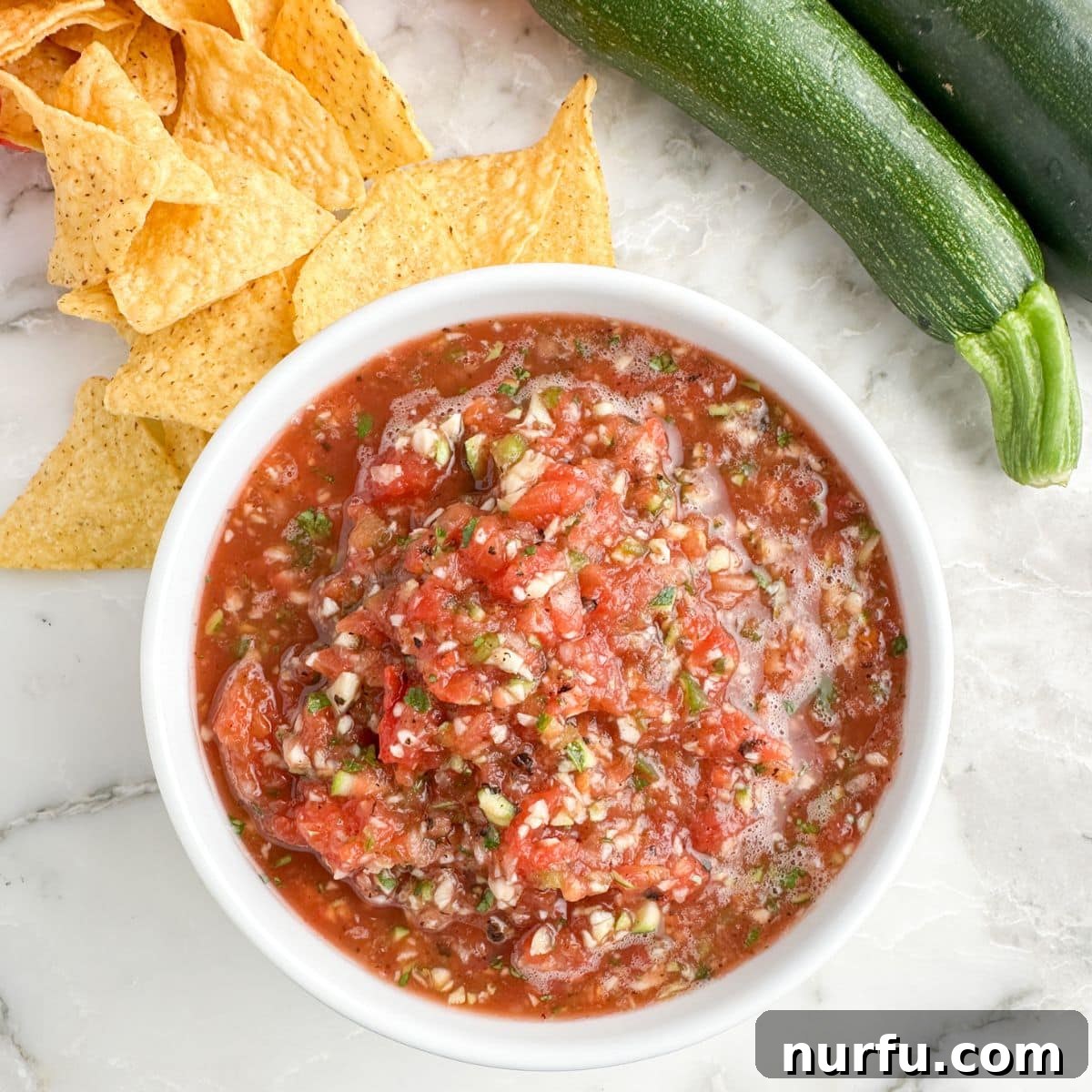 Zesty Zucchini Salsa 8 A beautifully presented bowl of homemade zucchini salsa, served with crispy tortilla chips, a fresh lime wedge, and a few slices of fresh zucchini for garnish.