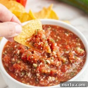Bowl of salsa with a tortilla chip dipping into it.