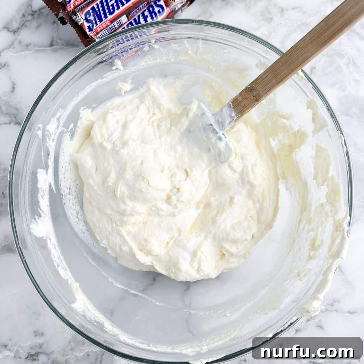 Snickers Caramel Apple Dream 5 Bowl of creamy pudding with whipped topping being stirred in with a spatula.