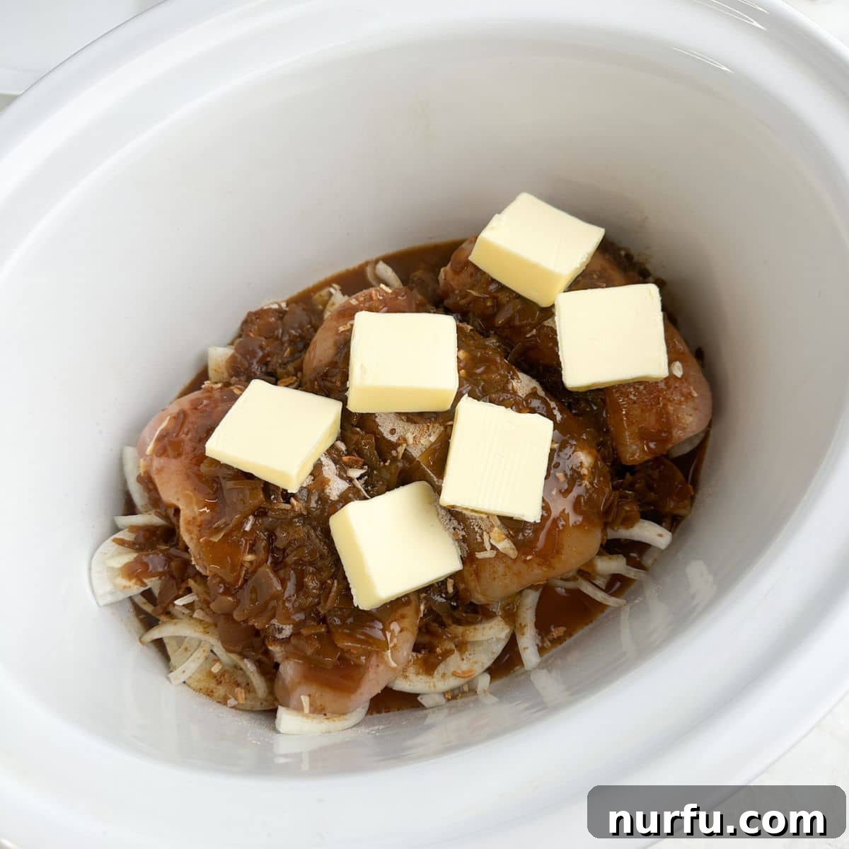 Caramelized French Onion Chicken 5 Slow cooker with onions, chicken, seasonings, and slices of butter.