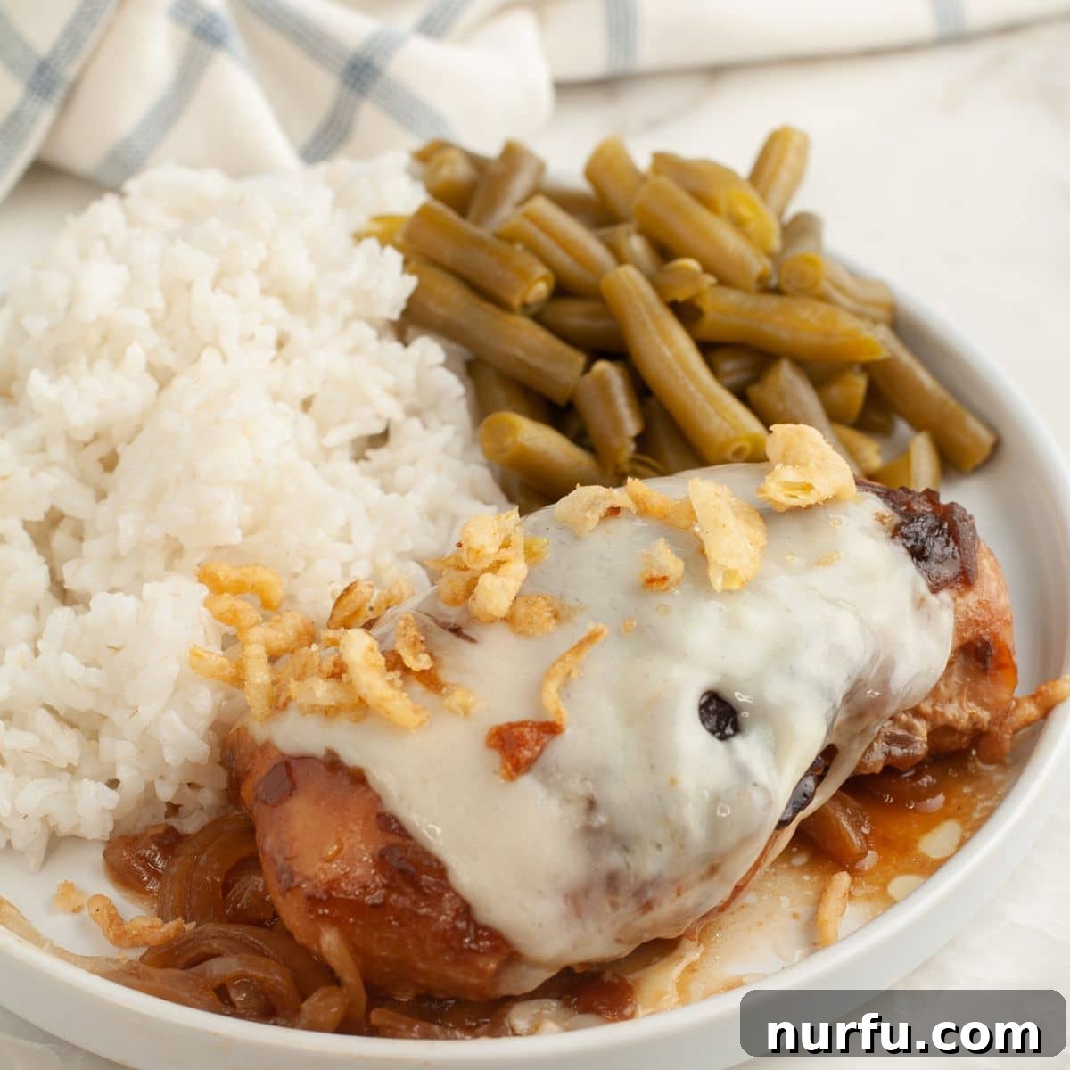 Caramelized French Onion Chicken 7 Plate with chicken topped with Swiss cheese, rice, and green beans.