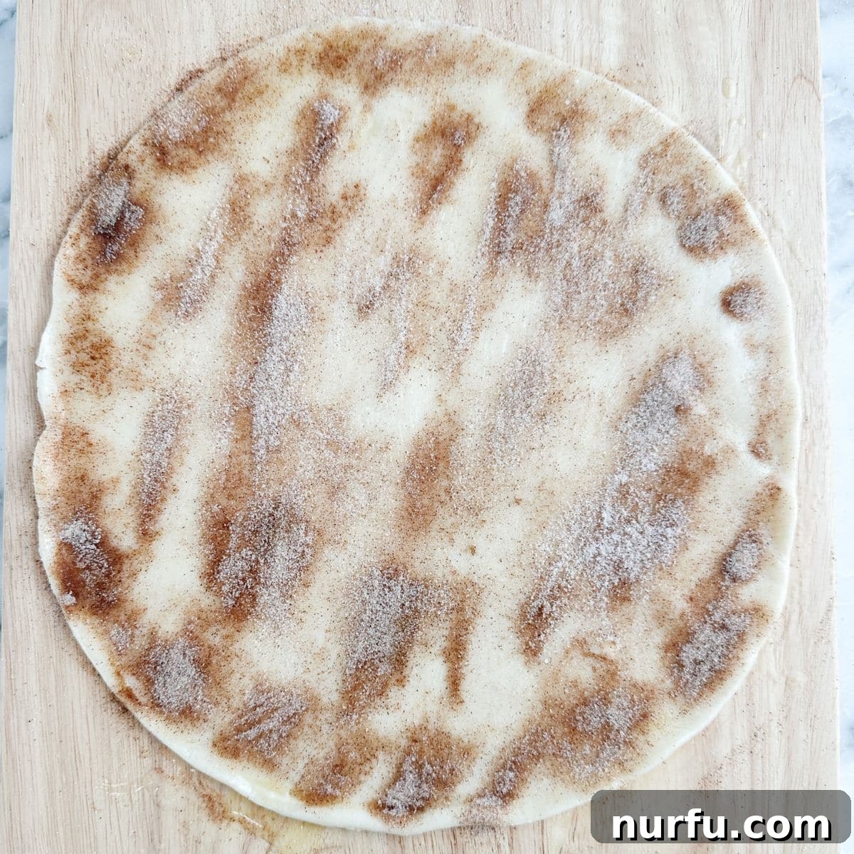 Unbaked pie crust liberally topped with a generous layer of cinnamon and sugar mixture, ready for cutting.