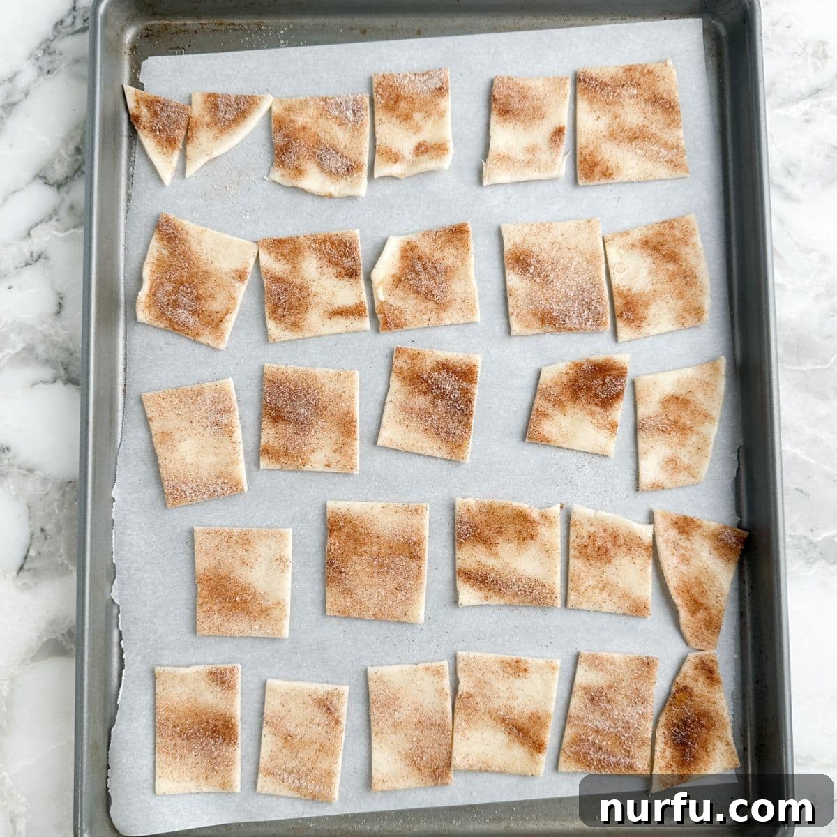 Sheet pan with uncooked pie crust chips neatly arranged, ready to go into the oven for baking.