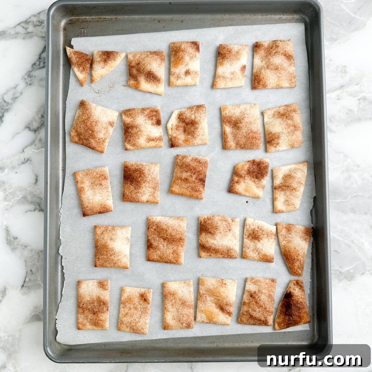 Freshly baked pie crust chips on a sheet pan, perfectly golden and crispy, cooling after coming out of the oven.