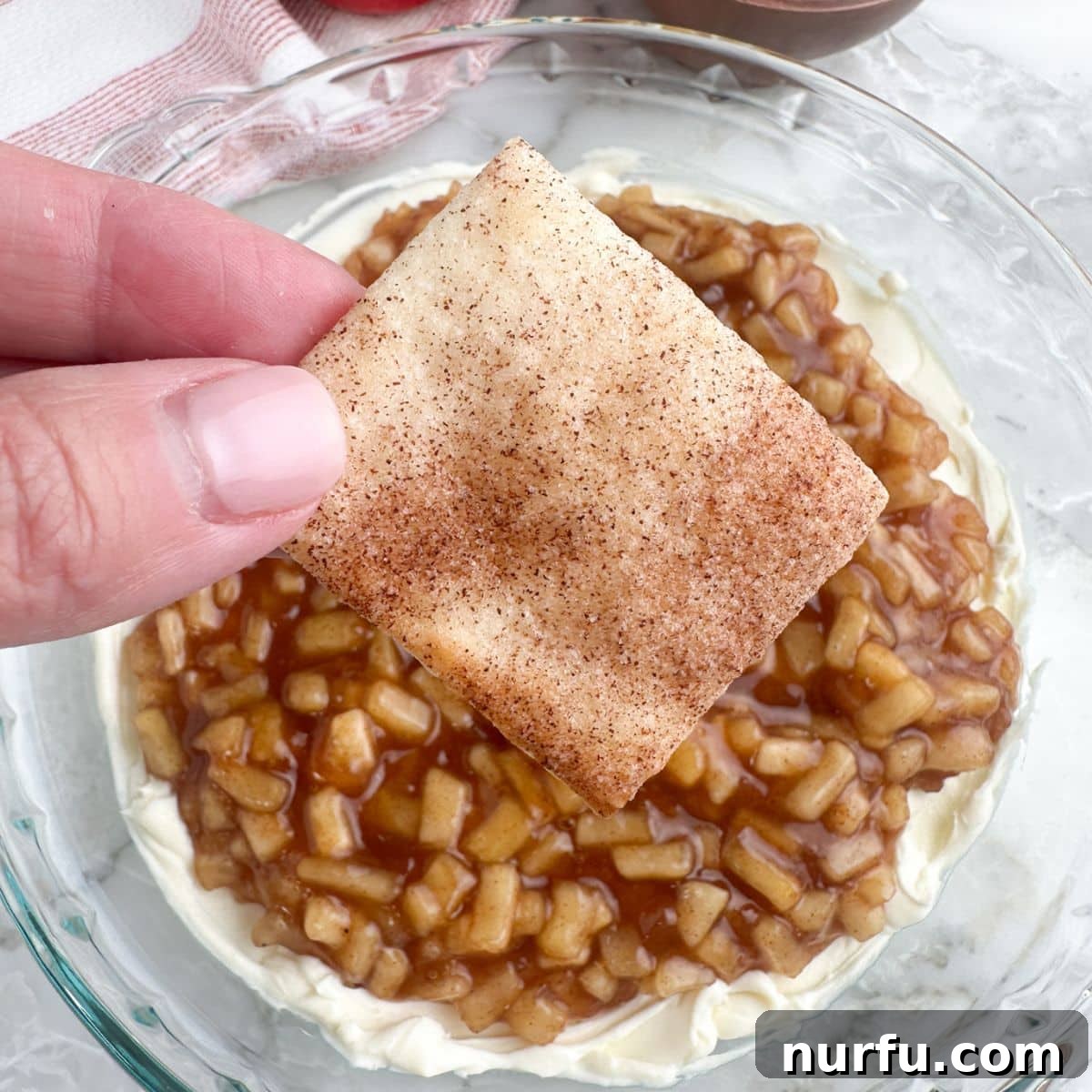 Hand holding a generous pile of perfectly baked cinnamon sugar pie crust chips, ready to be devoured.