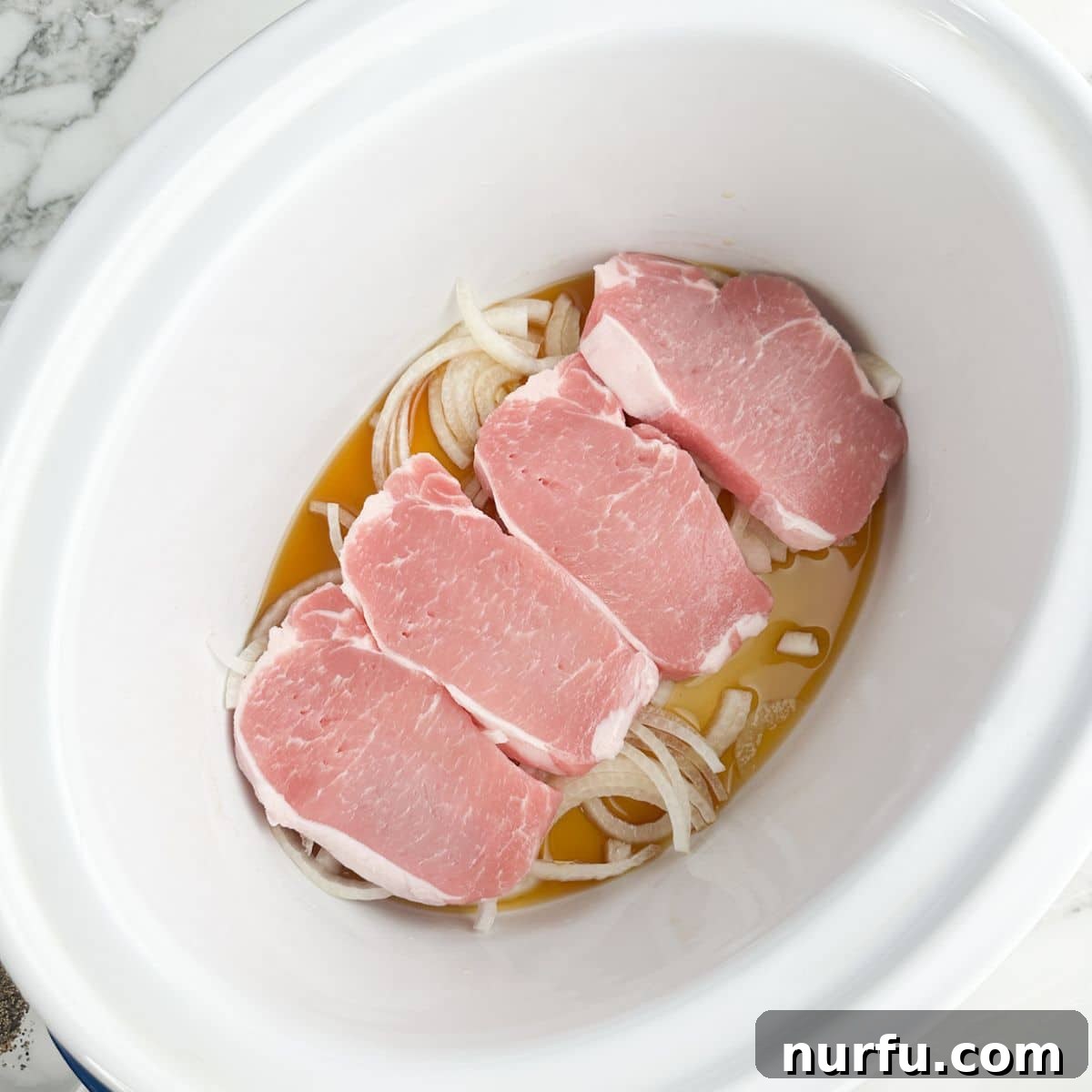 Tender Slow Cooker Pork and Apples 5 Slow cooker now layered with broth, onions, and succulent pork chops on top.
