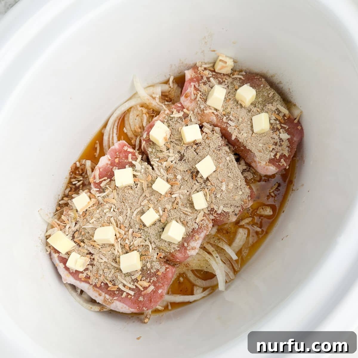 Tender Slow Cooker Pork and Apples 6 Slow cooker with onions, pork chops, seasonings, and pats of butter ready for the final layer.