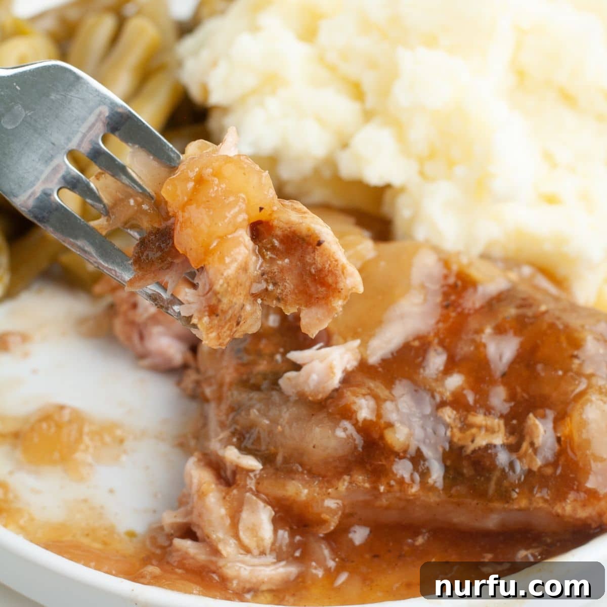 Tender Slow Cooker Pork and Apples 8 Close-up of a plate with a fork picking up a tender piece of pork chop and apple, highlighting the rich gravy.