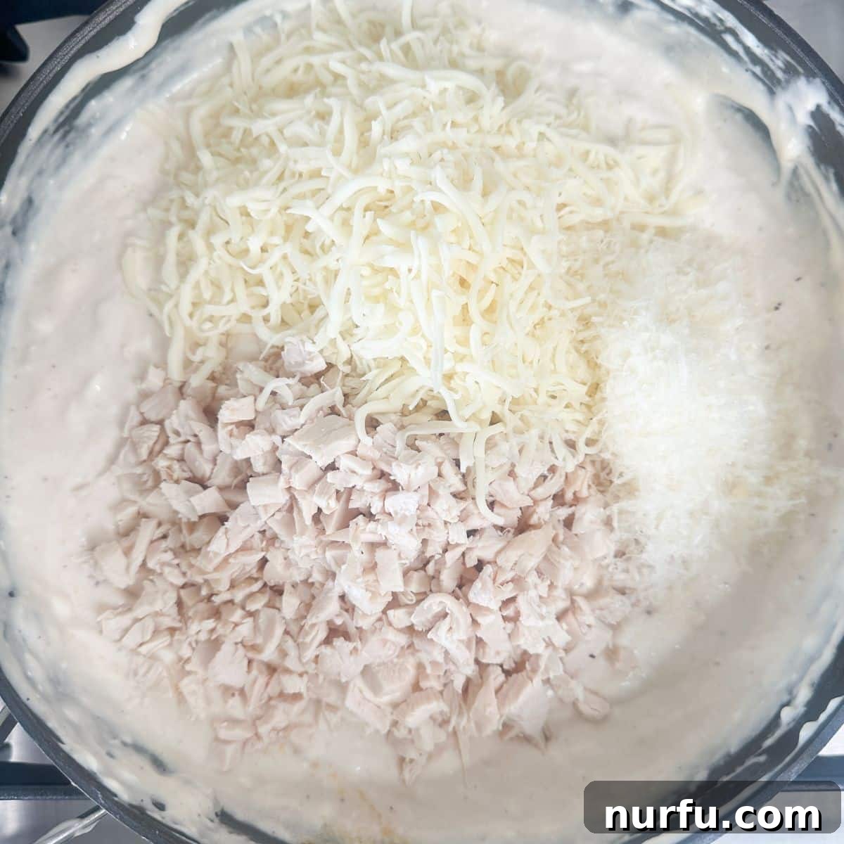 Ultimate Chicken Alfredo Dip 4 Saucepan with creamy Alfredo sauce, melted cream cheese, shredded chicken, and melted shredded cheese, ready to be transferred to a baking dish.