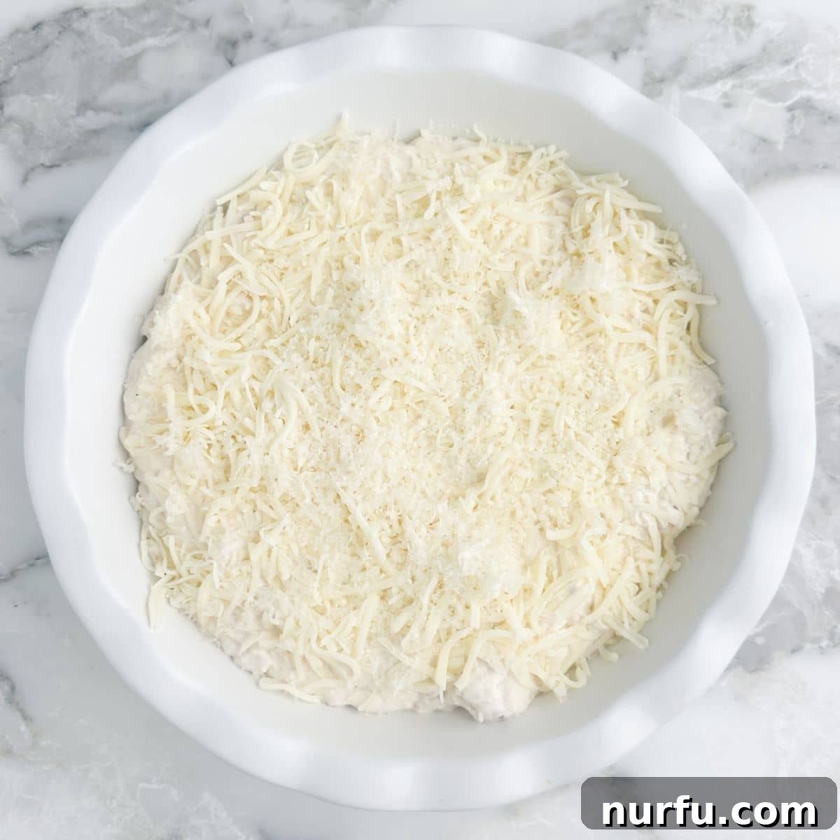 Ultimate Chicken Alfredo Dip 5 Baking dish filled with unbaked chicken alfredo dip, topped with extra shredded cheese, before going into the oven.