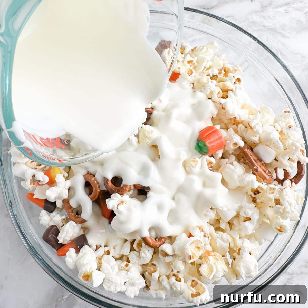 Sweater Weather Popcorn Mix 7 Bowl of popcorn, candy, and melted white chocolate being poured.