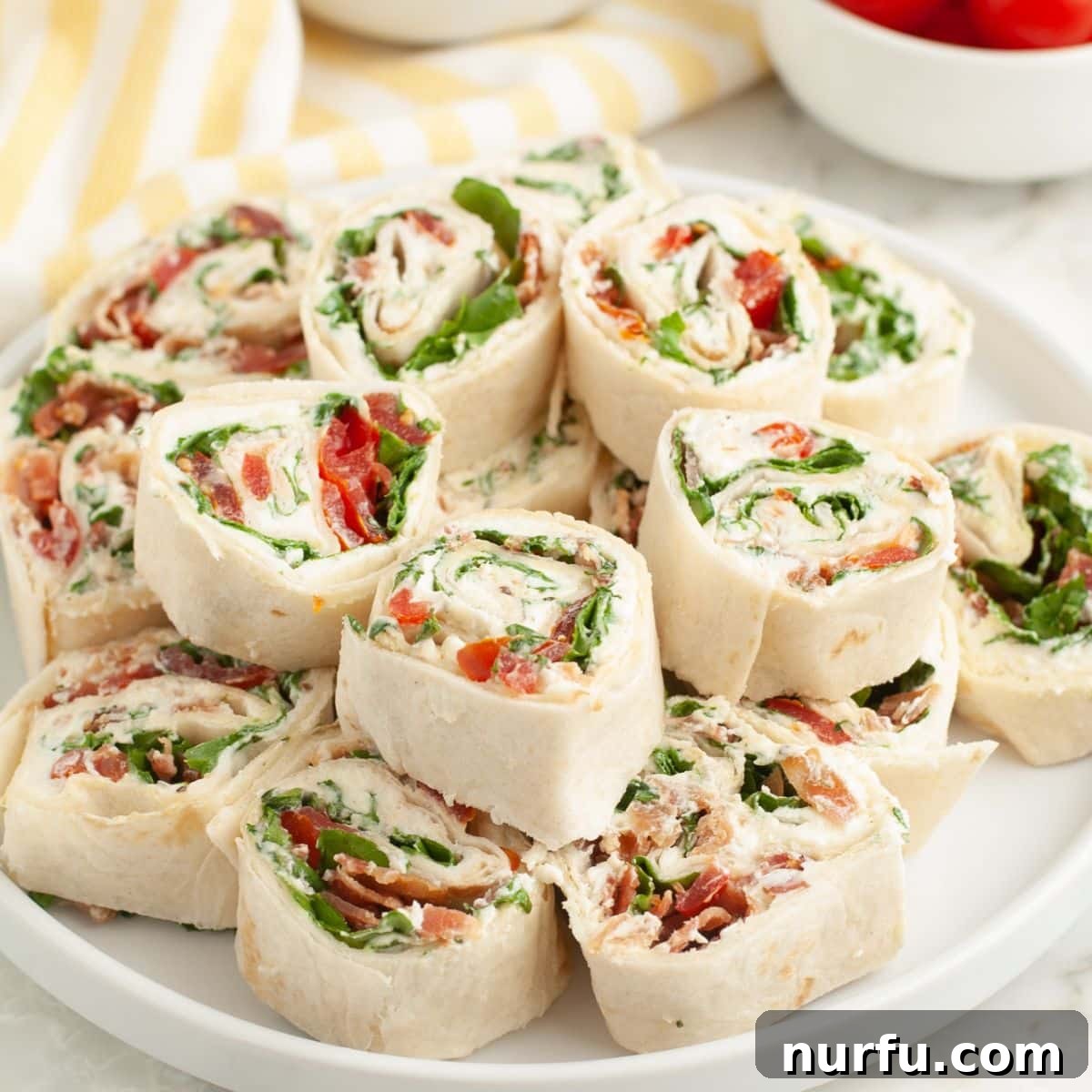 Creamy BLT Roll-Ups 8 A beautifully arranged plate of freshly sliced BLT pinwheels, showcasing their colorful spiral layers, ready to be served as an appetizer.