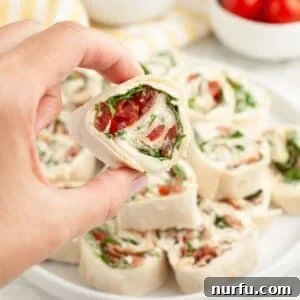 Hand holding a BLT pinwheel, showcasing the delicious layers inside.