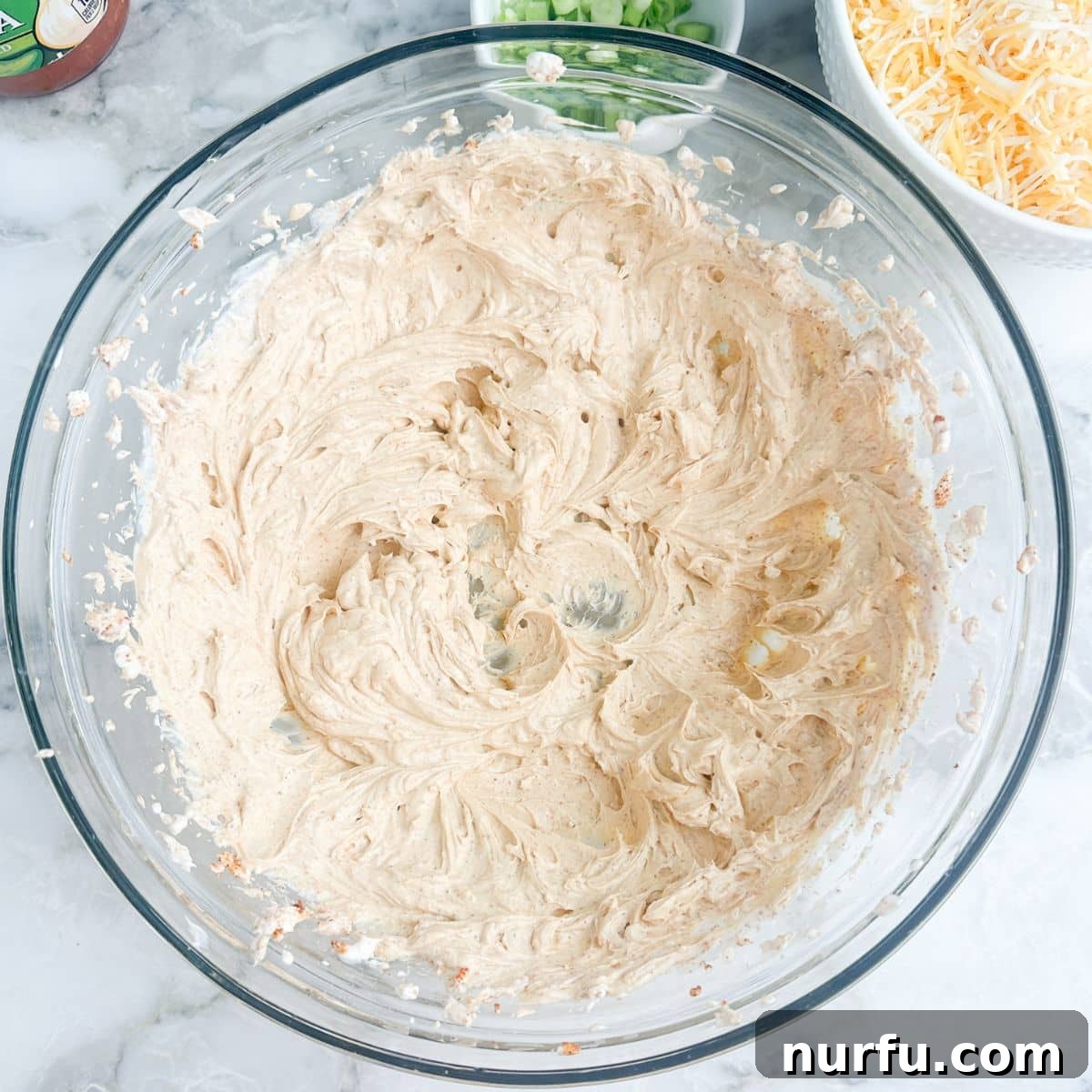 Stacked Salsa Sensation 4 A bowl containing softened cream cheese, sour cream, and taco seasoning, partially blended to show the creamy texture beginning to form.