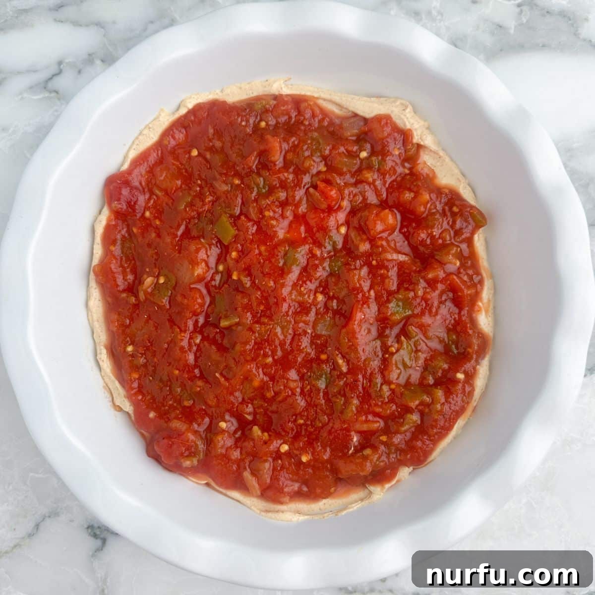 Stacked Salsa Sensation 6 A pie dish with the cream cheese layer covered by a vibrant red layer of chunky salsa, showing the distinct layers of the dip.