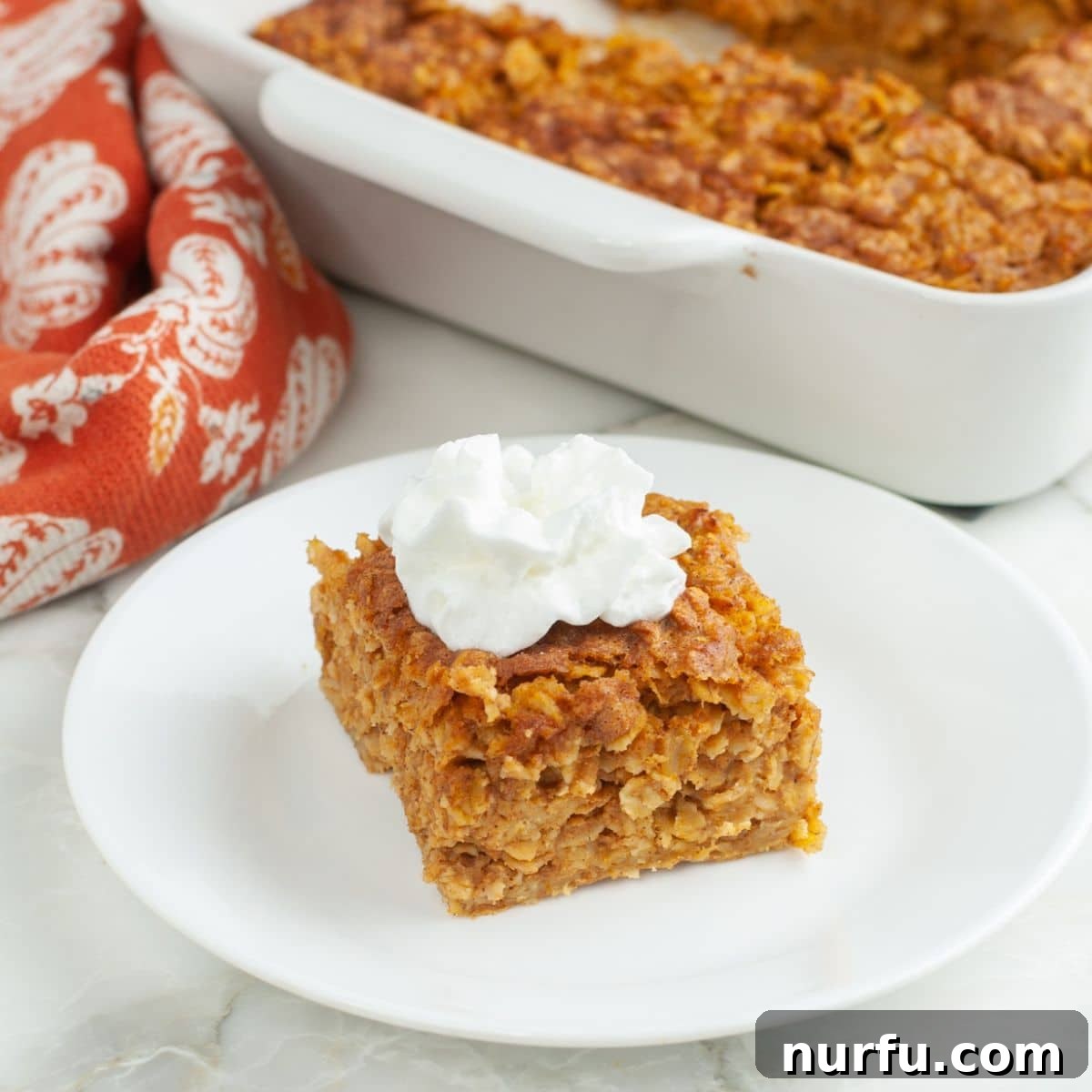 Warm Pumpkin Spice Baked Oatmeal 7 Plate with a piece of baked pumpkin oatmeal topped with a generous dollop of whipped cream, showcasing its appealing texture.
