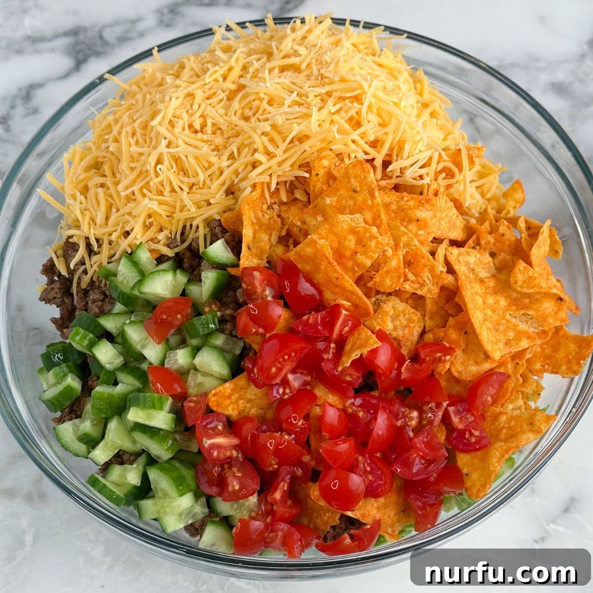 Catalina Kicked Taco Salad 7 Bowl of vibrant taco salad ingredients including shredded cheese, Doritos, diced cucumbers, and tomatoes.
