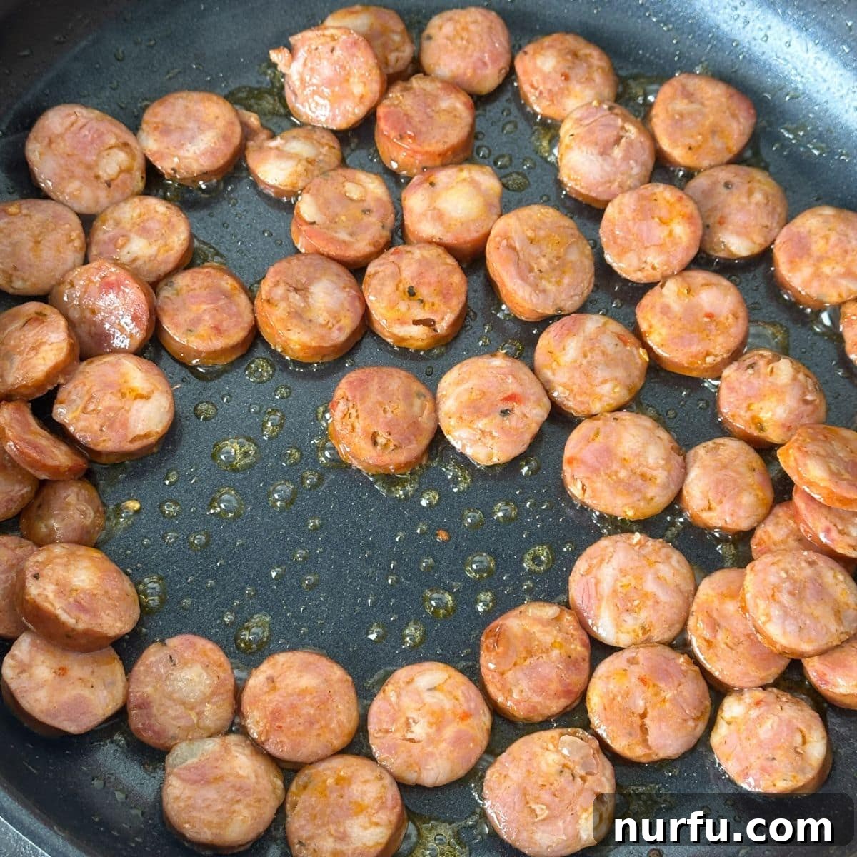 Close-up of a skillet filled with sliced andouille sausage browning evenly, preparing for the next step of the Cajun pasta recipe.