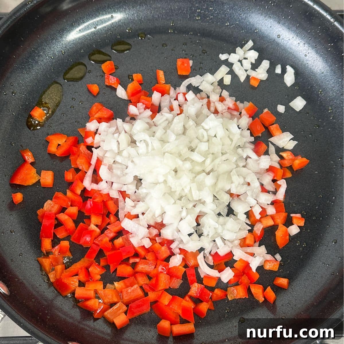 Diced red bell peppers and onions sizzling in a skillet, softened and fragrant after being sautéed in the remaining sausage grease.