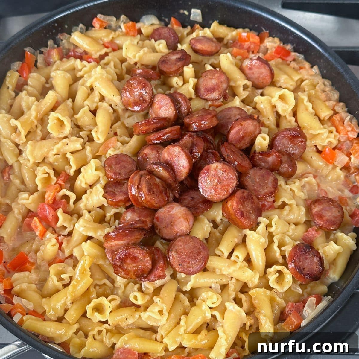 The finished Cajun sausage pasta dish, featuring tender pasta, browned andouille sausage, and a rich, creamy sauce, all mixed together in a large skillet.