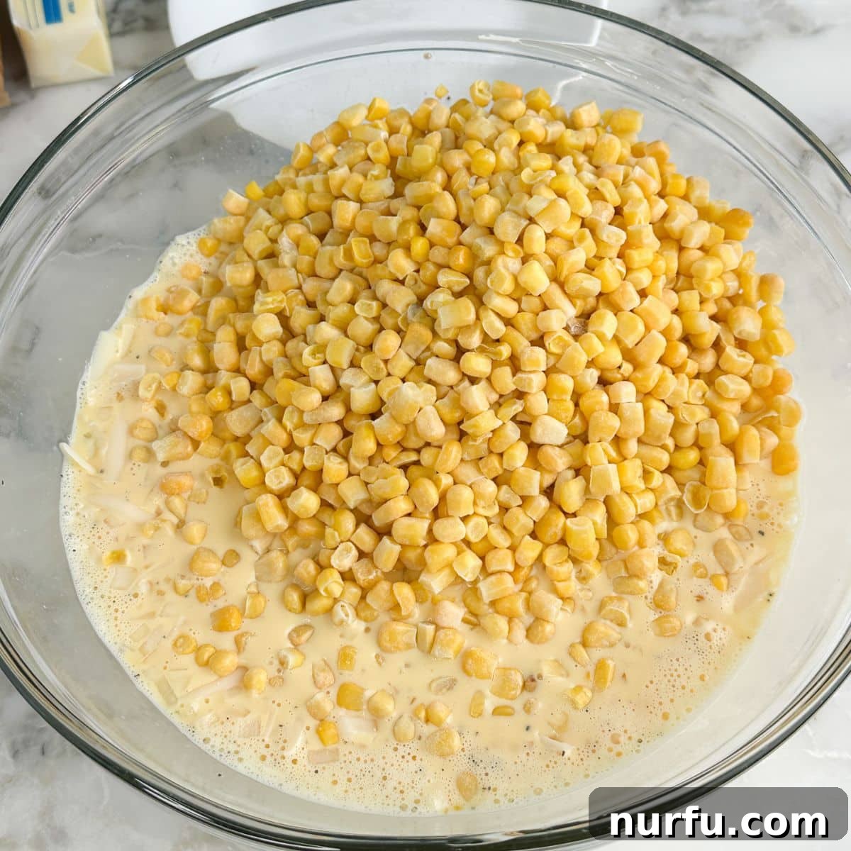 Creamy Swiss Corn Gratin 4 A mixing bowl filled with beaten eggs, evaporated milk, and corn, ready to be combined with cheese and onion.