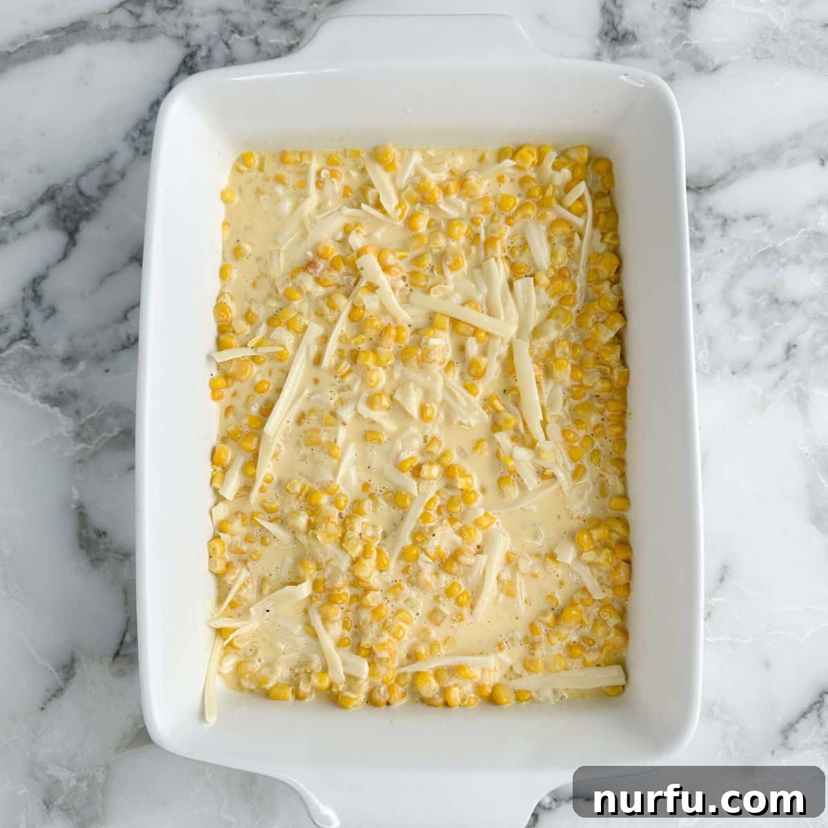 Creamy Swiss Corn Gratin 5 An unbaked corn casserole mixture spread evenly in a glass baking dish, before topping is added.