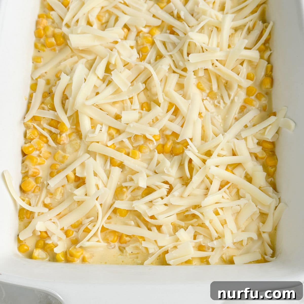 Creamy Swiss Corn Gratin 6 A casserole dish with corn mixture topped with a generous layer of shredded Swiss cheese, before the cracker topping.