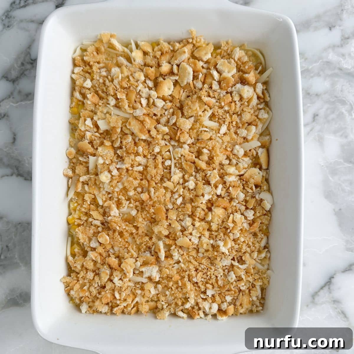 Creamy Swiss Corn Gratin 7 A baking dish with corn casserole topped with a golden layer of crumbled, buttered crackers, ready for the oven.