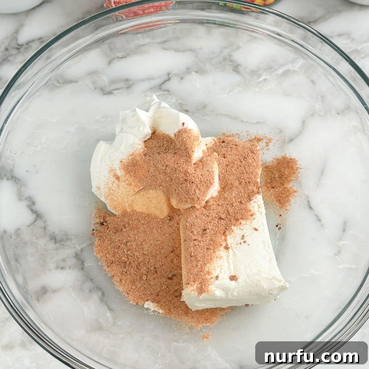 A bowl containing cream cheese, sour cream, and ranch seasoning, being blended with an electric mixer.