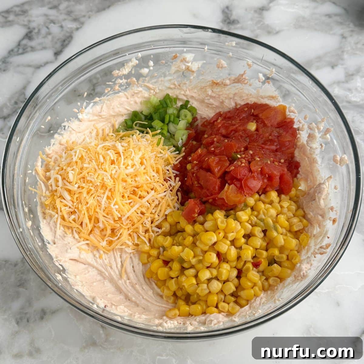 A bowl of creamy dip with shredded cheese, corn, and Rotel tomatoes stirred in.