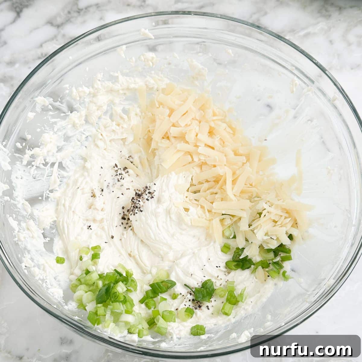 A bowl containing a creamy mixture of softened cream cheese, shredded Parmesan cheese, and diced green onion.